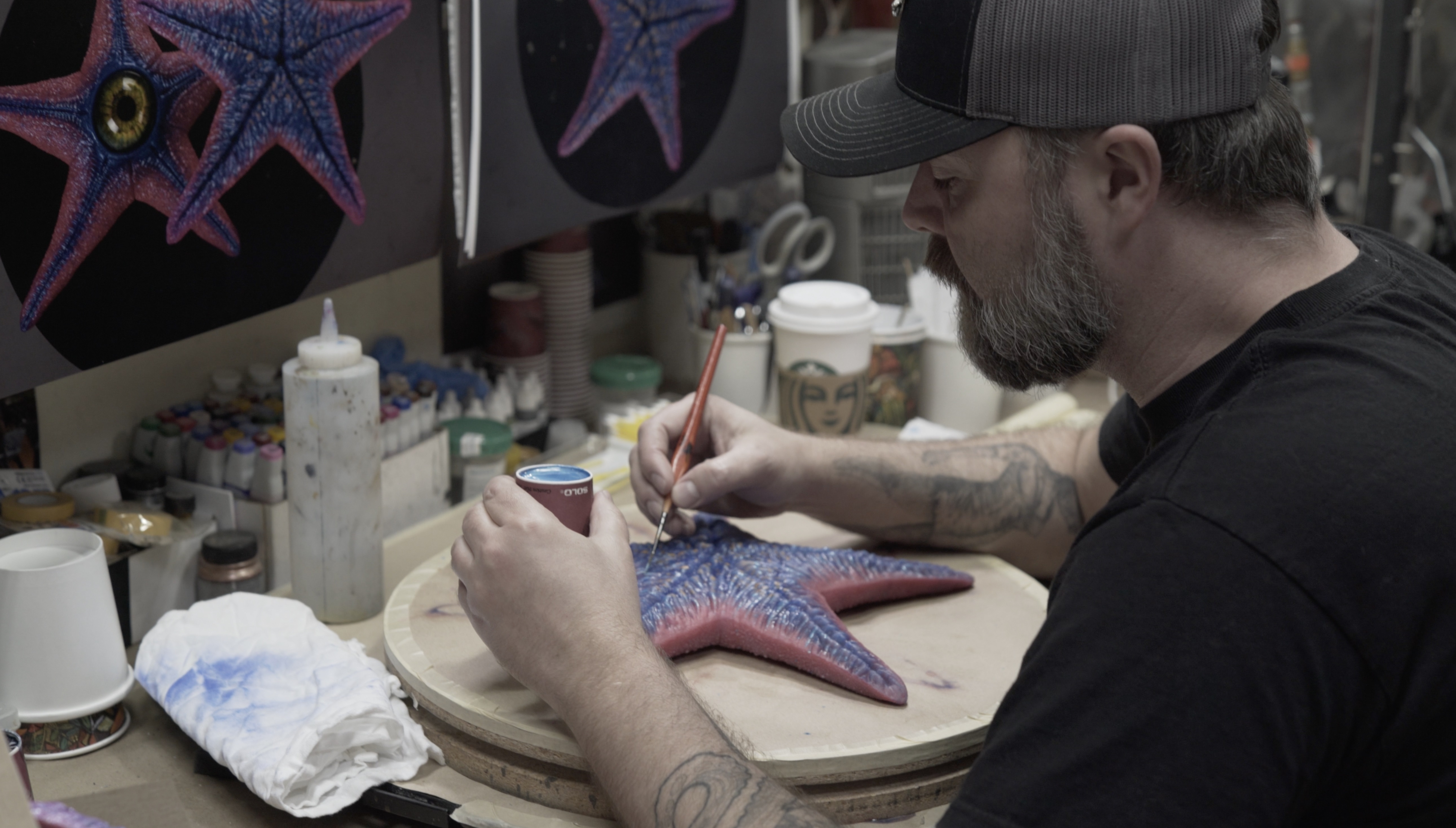 Legacy artist Ryan Pintar paints one of the 'hero' silicone starfish masks. Note the paint reference artwork above the workbench. Image courtesy Legacy Effects/Warner Bros.
