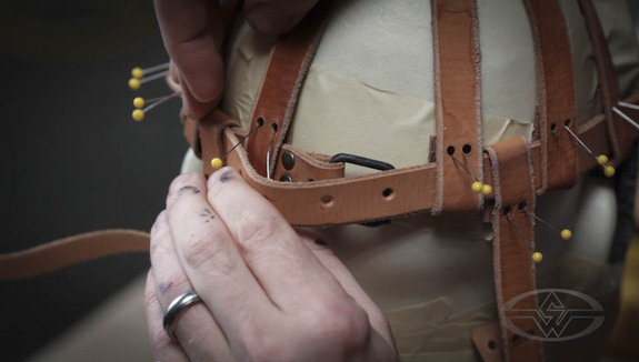 Using pins to keep the straps in place, Bruce affixes burnished buckles and rivets to the holes he's punched in the leather.